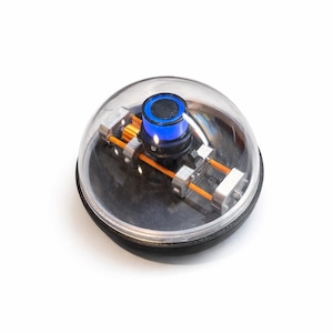 May include: A futuristic, spherical device with a clear, dome-shaped cover. Inside, there's a blue-lit component and a network of orange and silver parts. The base is black, and the whole object sits against a white background.