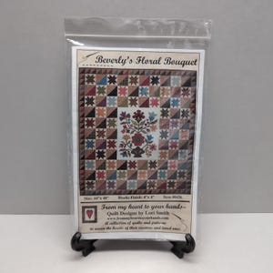 May include: A quilt pattern titled "Beverly's Floral Bouquet" featuring a floral design in the center and star-shaped blocks. The pattern is 44" x 48" and includes the text "From my heart to your hands... Quilt Designs by Lori Smith."