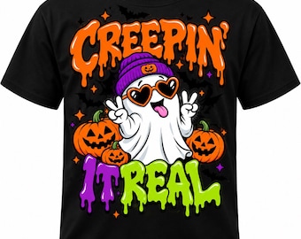 May include: A black t-shirt featuring a graphic of a white ghost wearing a purple beanie and heart-shaped sunglasses, making a peace sign. The text CREEPIN IT REAL is printed in orange and green, surrounded by orange jack-o'-lanterns and small stars.
