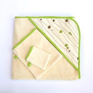 Può includere: Un set di tre asciugamani color crema con bordino verde. L'asciugamano con cappuccio presenta un motivo bianco e verde con piccoli gufi marroni.