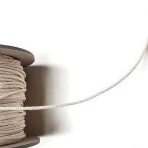 May include: A spool of natural white cotton cord, with a length of cord extending from the spool.