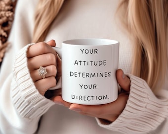 Puede incluir: Taza de cerámica blanca con texto negro que dice "YOUR ATTITUDE DETERMINES YOUR DIRECTION."