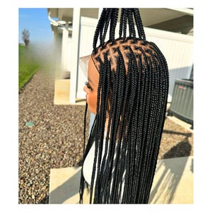 May include: A black braided wig with long, straight strands. The wig is styled in a box braid pattern and is made with synthetic hair.