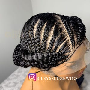 Könnte beinhalten: Eine schwarze geflochtene Perücke mit einem Dutt am Hinterkopf. Die Perücke weist komplizierte Cornrow-Muster und eine Spitze vorne auf. Der Instagram-Handle @BILSYS SLUXE WIGS ist unten im Bild zu sehen.
