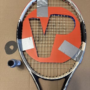 May include: A white and black tennis racket with a large orange stencil of the letter V taped to the strings using silver duct tape. A small blue paint container sits to the left of the racket frame, which features the text Carbon Matrix.