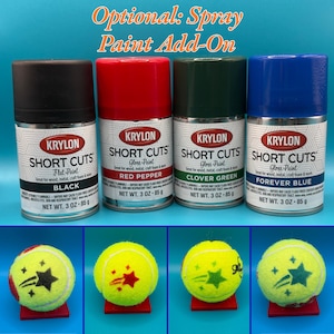 May include: Four cans of Krylon Short Cuts paint in black, red pepper, clover green, and forever blue, each 3 oz, alongside four yellow tennis balls, each featuring a unique star-shaped graphic print in a color matching one of the paint cans.