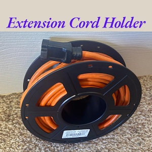 May include: Black extension cord holder with an orange cord. The cord is coiled around a black reel. The text "Extension Cord Holder" is in purple above the reel.