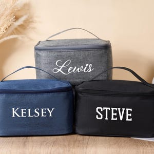 以下が含まれることがあります： ネイビーブルー、グレー、ブラックの3つのパーソナライズされた化粧品バッグ。各バッグにはハンドルと、白で印刷された名前「Kelsey」、「Lewis」、「Steve」が付いています。バッグは長方形で、ジッパーで開閉します。