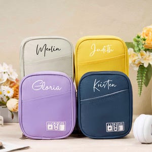 Könnte beinhalten: Vier kleine, Reißverschluss-Reisetaschen in Hellgrau, Gelb, Lila und Marineblau. Jede Tasche hat einen Namen in weißer Schrift: Merlin, Judith, Gloria und Kristen. Die Taschen haben eine Vordertasche und eine kleine Grafik mit Stecker, Akku und anderen Tech-Symbolen.