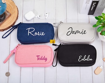 Può includere: Quattro pochette con cerniera in tessuto di diversi colori e nomi personalizzati. Le pochette sono blu navy, grigio chiaro, rosa e nero. I nomi sono Rosie, Jamie, Teddy ed Eulalia.