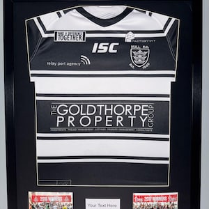 May include: Framed black and white sports jersey with the text "MAKE A DIFFERENCE TOGETHER" and "THE GOLDTHORPE PROPERTY GROUP". Includes two small photos labeled "2016 WINNERS" and "2017 WINNERS". A white rectangle reads "Your Text Here".