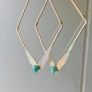 May include: Gold geometric earrings with a teardrop-shaped pendant and a light blue gemstone.