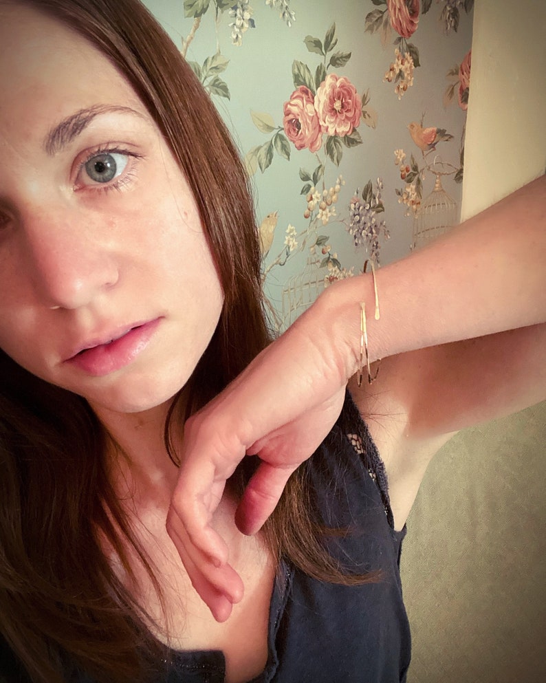 May include: A close-up of a woman's face with brown hair. She is wearing a gold bracelet on her wrist. The background is a floral wallpaper.