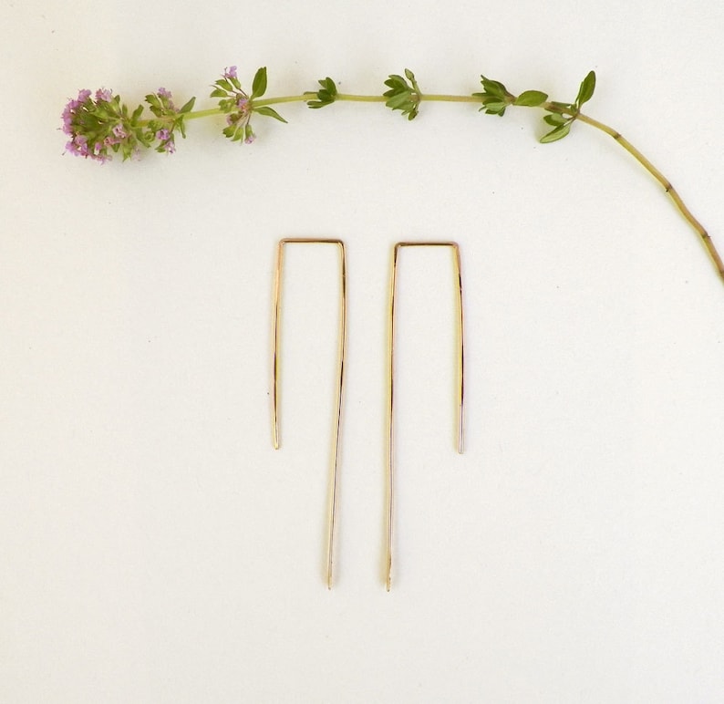 May include: A pair of gold-toned, minimalist earrings with a simple, rectangular shape.