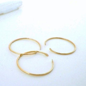 Puede incluir: Tres anillos de color dorado, cada uno con un dise&ntilde;o simple de c&iacute;rculo abierto ligeramente redondeado. Los anillos est&aacute;n dispuestos en un patr&oacute;n suelto y superpuesto.