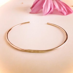 May include: A simple, hammered gold bangle bracelet. The bracelet is made of a single piece of metal and has a smooth, polished finish.