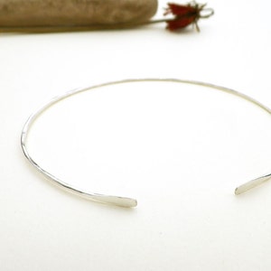 May include: A simple silver choker necklace with a hammered finish. The necklace is open in the back and has a slightly curved shape.
