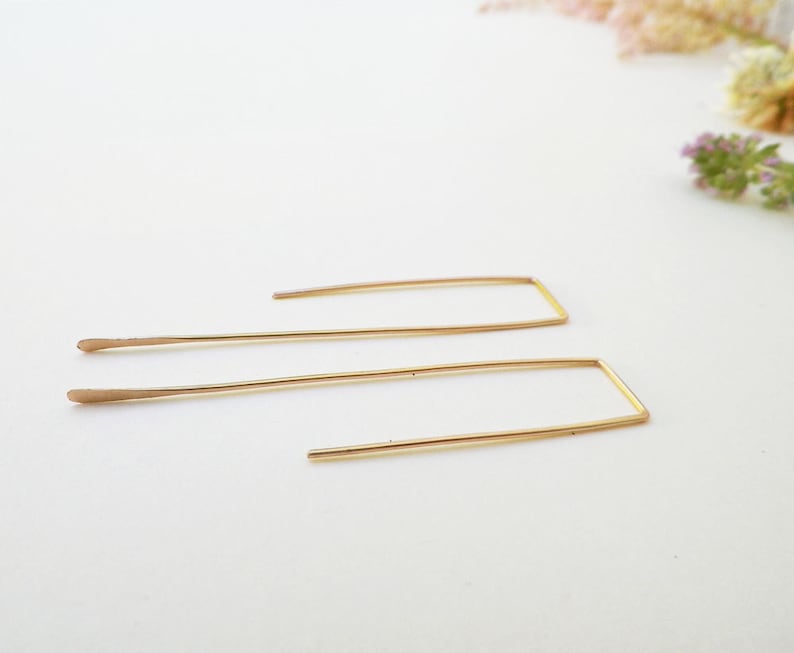 May include: A pair of gold-toned rectangle shaped earrings with a thin wire design.