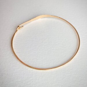 K&ouml;nnte beinhalten: Ein zartes goldfarbenes Armband mit geh&auml;mmerten Textur. Das Armband ist ein d&uuml;nner, offener Kreis mit einem kleinen Verschluss. Das Design ist schlicht und elegant, f&uuml;r den Alltag geeignet. Der Durchmesser des Armbands betr&auml;gt ca. 6,35 cm.