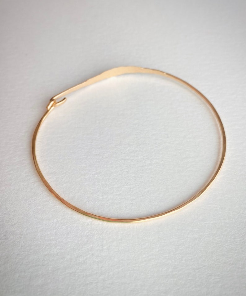 K&ouml;nnte beinhalten: Ein zartes goldfarbenes Armband mit geh&auml;mmerten Textur. Das Armband ist ein d&uuml;nner, offener Kreis mit einem kleinen Verschluss. Das Design ist schlicht und elegant, f&uuml;r den Alltag geeignet. Der Durchmesser des Armbands betr&auml;gt ca. 6,35 cm.