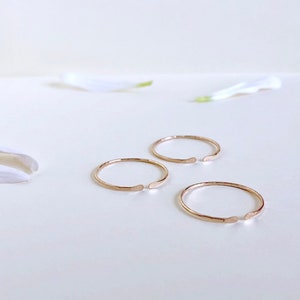 Puede incluir: Tres anillos abiertos de color dorado sobre una superficie blanca. Los anillos son finos y tienen una textura martillada.
