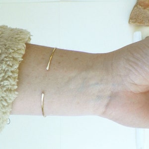 May include: A simple gold bangle bracelet on a person's wrist.