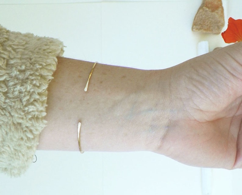 May include: A simple gold bangle bracelet on a person's wrist.