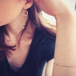 May include: A woman wearing a black shirt with a gold chain and circle earrings.