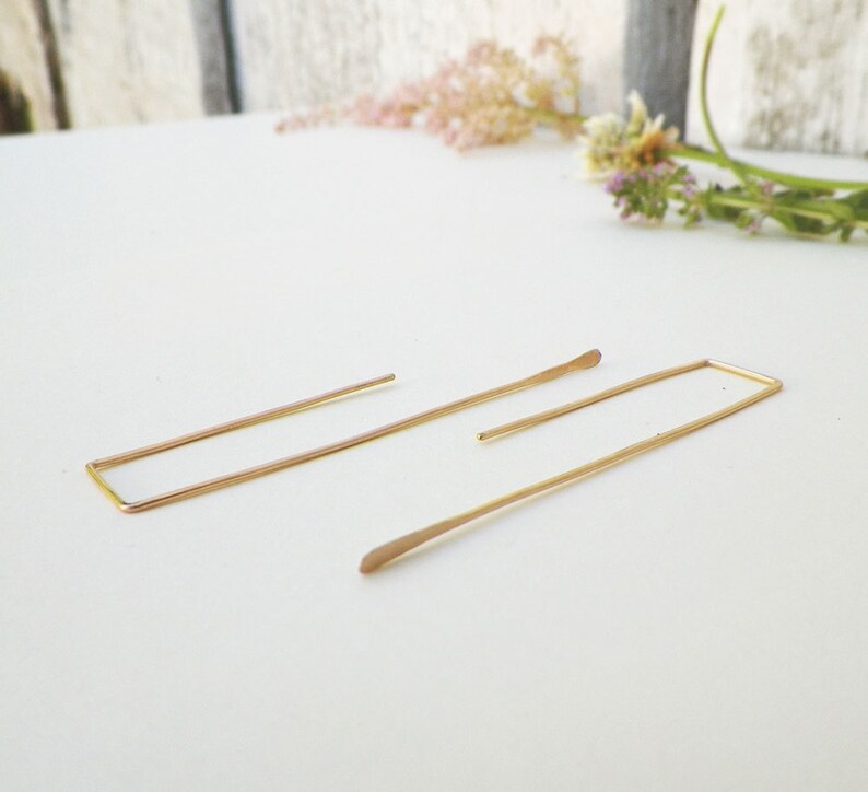 May include: A pair of gold minimalist earrings with a rectangular shape. The earrings are made of thin wire and have a simple, modern design.