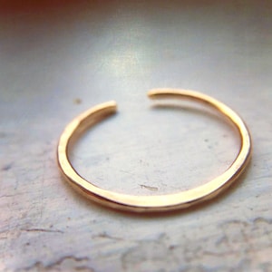 May include: A gold-toned, hammered, open ring. The ring is made of metal and has a smooth, rounded finish.