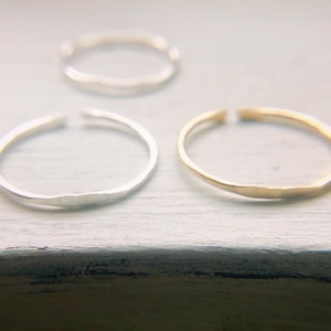 May include: Three simple, hammered metal rings. One ring is silver, one is gold, and one is a lighter shade of silver.