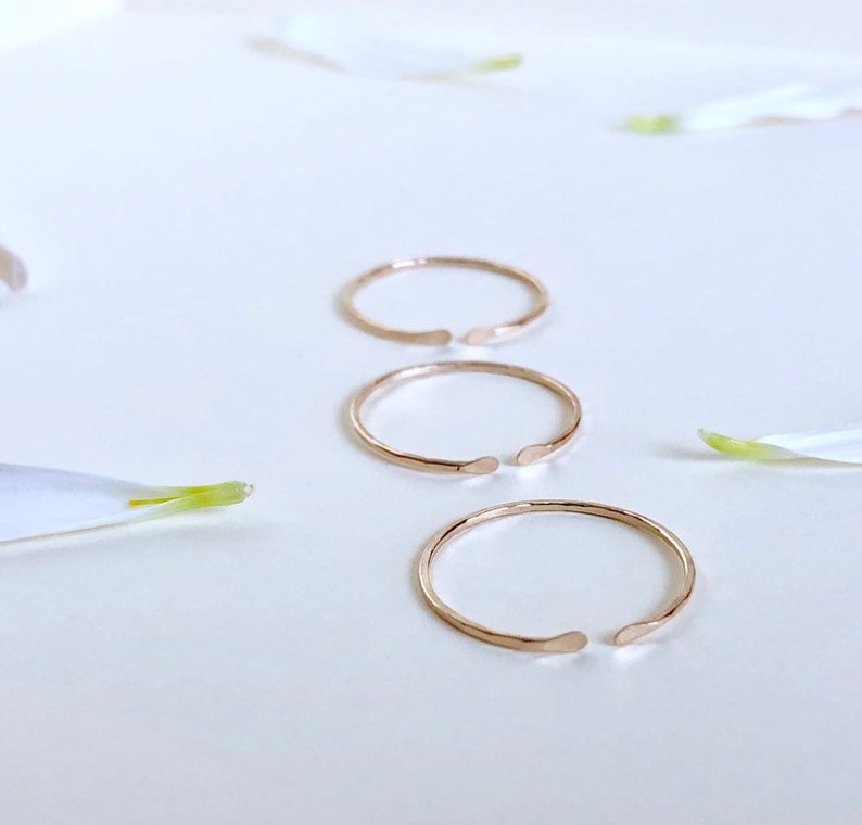 Puede incluir: Tres anillos abiertos de color dorado sobre una superficie blanca. Los anillos est&aacute;n hechos de metal fino y tienen una textura ligeramente martillada.