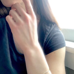 May include: A gold bracelet on a person's wrist. The bracelet is thin and delicate, and it is made of a simple, minimalist design.