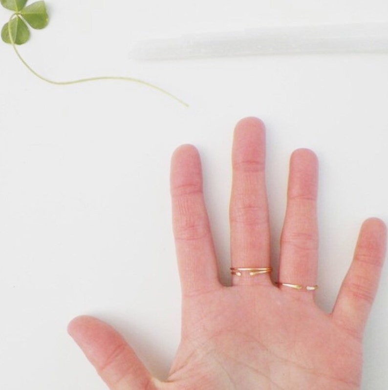 Puede incluir: Una mano con tres anillos finos de oro en los dedos medio y anular.