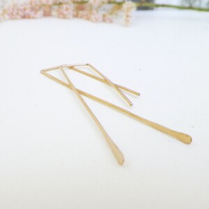 May include: A pair of gold-toned geometric earrings with a simple, minimalist design. The earrings are made of thin, straight wires that are bent into a rectangular shape.