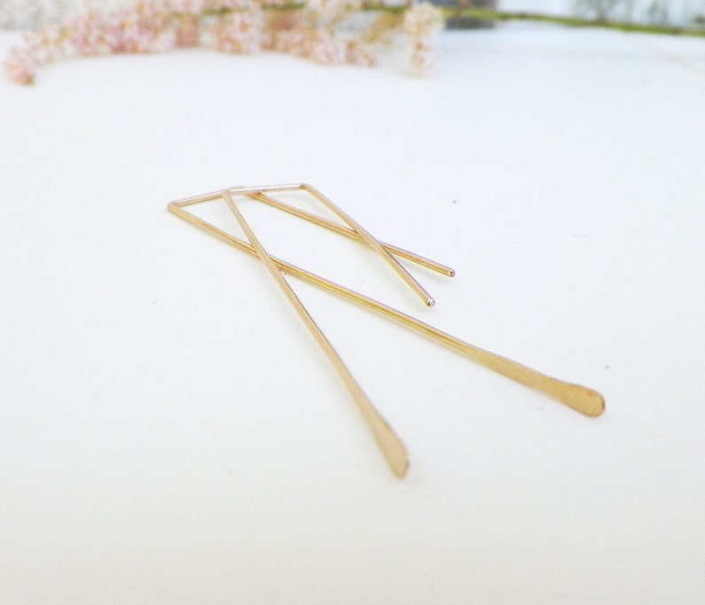 May include: A pair of gold-toned geometric earrings with a simple, minimalist design. The earrings are made of thin, straight wires that are bent into a rectangular shape.