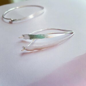 K&ouml;nnte beinhalten: Zwei Schmuckst&uuml;cke aus Silber. Eines ist ein Armband, das andere ein Paar Ohrringe. Die Ohrringe haben ein einzigartiges Design mit einer langen, strukturierten, blattartigen Form. Das Armband ist ein einfaches, d&uuml;nnes Band. Beide Teile haben ein gl&auml;nzendes, metallisches Finish.
