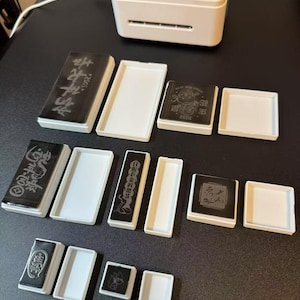 May include: A white rectangular device labeled "mint" with a small circle on the top.  The device is surrounded by 12 white rectangular and square frames, some of which contain black and white stamps with Chinese characters and images.