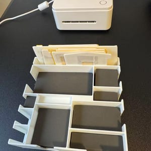 May include: A white Silhouette Mint machine with the word "mint" printed on the top, and a white organizer with multiple compartments and gray foam inserts. The organizer is designed to hold various crafting supplies.