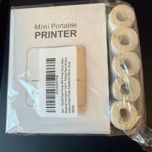 May include: A white box labeled Mini Portable PRINTER with a line drawing of the device, featuring a barcode sticker with text including New - Doodle Dash Printer Mini Printer Sticker Maker Bluetooth Connection Cell P... Printing Paper Wireless.