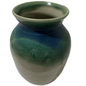 May include: A handmade ceramic vase with a rounded body and a slightly flared rim. The vase features a gradient of colors, transitioning from a light beige at the base to shades of green and blue towards the top. The interior is a light beige color.