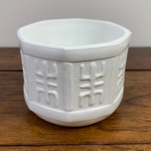 May include: A white milk glass bowl featuring a hexagonal shape and a repeating embossed geometric pattern around the exterior. The bowl has a smooth, glossy finish and a wide, open top, showcasing a clean, solid white colour throughout.