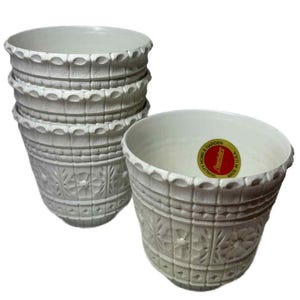 May include: A set of six off-white ceramic flower pots. The pots have a textured, embossed design with floral and geometric patterns. Each pot has a scalloped rim. One pot has a red and gold sticker.