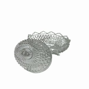 May include: A clear, vintage glass candy dish with a lid. The dish and lid are decorated with a textured pattern of small, raised dots and a scalloped edge. The lid is partially open, revealing the interior of the dish.