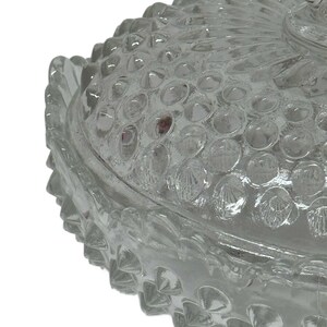 May include: Clear glass candy dish with a textured, bubble-like pattern on the lid and base. The edges of the dish have a scalloped design. The dish is likely vintage and suitable for decorative use.
