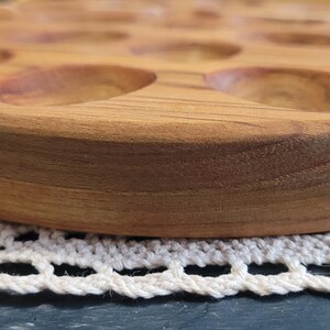May include: A wooden egg tray with 12 individual compartments for holding eggs. The tray is made of light brown wood and has a smooth, rounded edge.