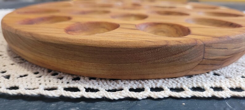 May include: A wooden egg tray with 12 individual compartments for holding eggs. The tray is made of light brown wood and has a smooth, rounded edge.