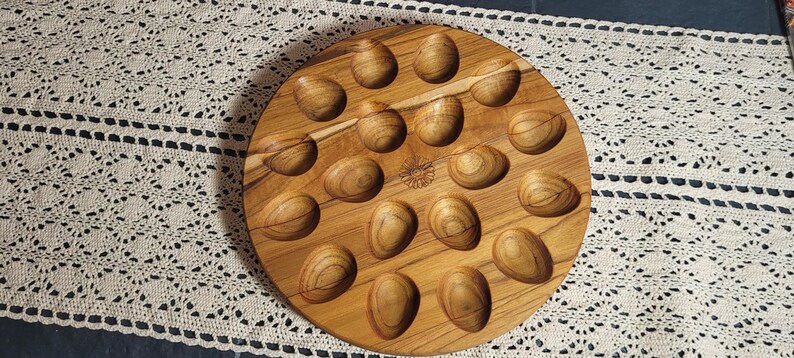 May include: A wooden egg tray with 18 individual indentations for holding eggs. The tray is circular and has a natural wood finish.