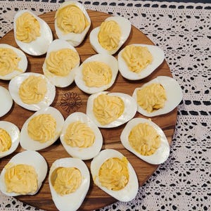 May include: A wooden serving tray with 18 deviled eggs arranged in a circular pattern. The eggs are peeled and sliced in half, with the yolks scooped out and mixed with a creamy filling.