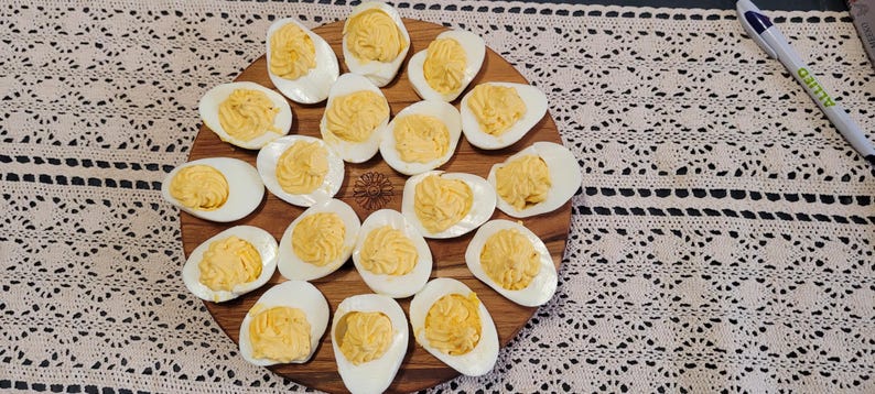 May include: A wooden serving tray with 18 deviled eggs arranged in a circular pattern. The eggs are peeled and sliced in half, with the yolks scooped out and mixed with a creamy filling.